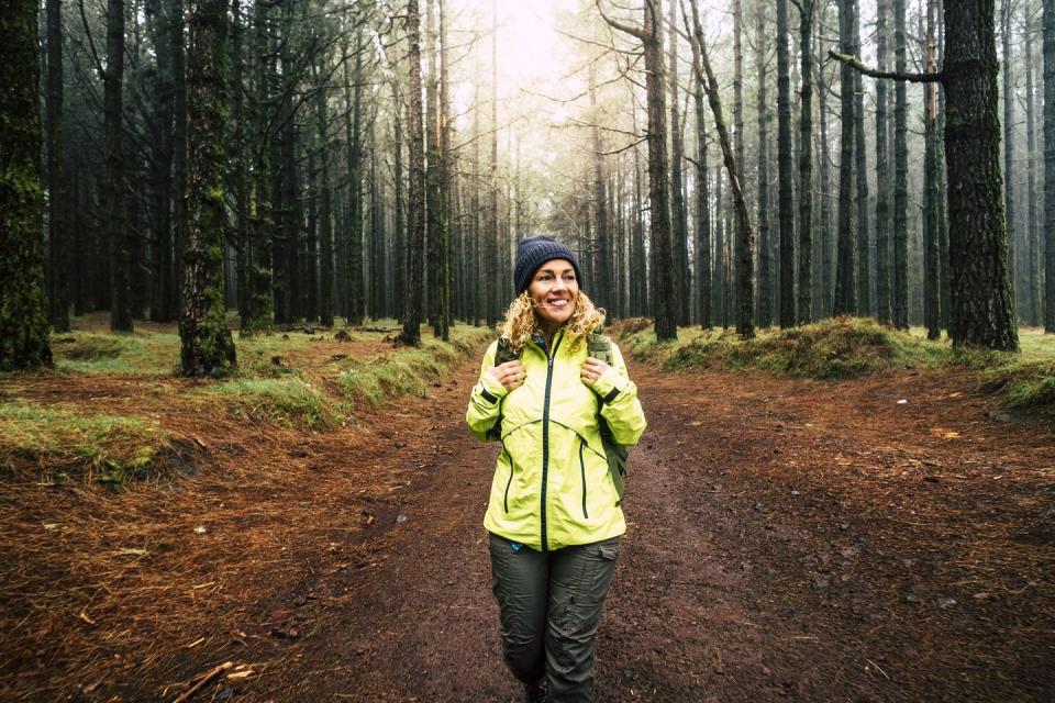 happy hiker caucasian woman smile and enjoy the nature walking in a forest with high trees alternative outdoor leisure activity and vacation lifestyle sun in backlight and mist concept