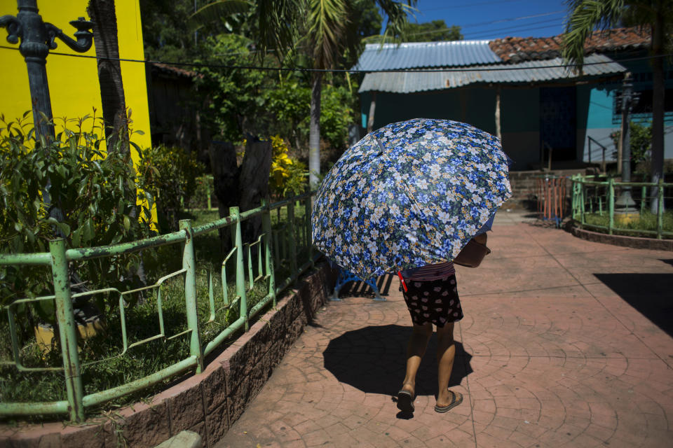 In this Aug. 18, 2018 photo, a woman shades herself from the sun with an umbrella in the central square in Intipuca, El Salvador. Residents say they don't migrante to the U.S. to flee gang violence, but instead are seeking upward mobility. (AP Photo/Rebecca Blackwell)