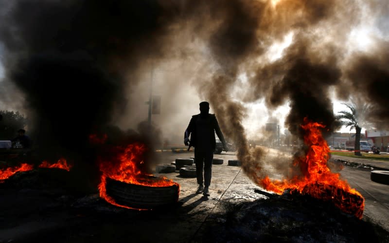 A man walks between burning tires during ongoing anti-government protests in Najaf