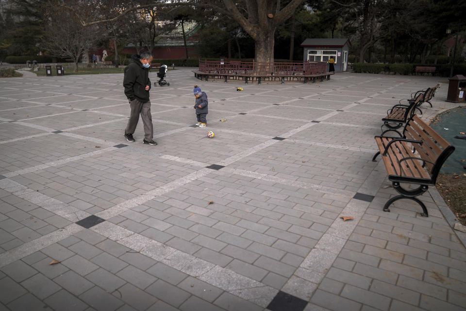 A man wearing a face mask plays a ball with a child at an area used to be crowded with residents at a public park in Beijing, Monday, Dec. 12, 2022. China will drop a travel tracing requirement as part of an uncertain exit from its strict "zero-COVID" policies that have elicited widespread dissatisfaction. (AP Photo/Andy Wong)