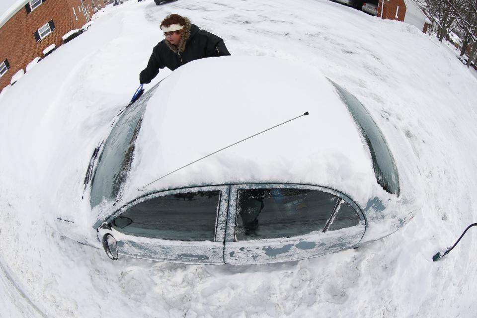 In an image made with a fisheye lens, Marguerite Johnston uncovers her car in Grosse Pointe, Mich., Monday, Jan. 6, 2014. Michigan residents are preparing for diving temperatures as they dig out from more than 15 inches of snow in places. (AP Photo/Paul Sancya)