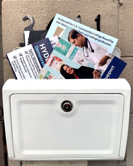 Campaign mail bursts out the top of a home's vertical mailbox attached to a wall