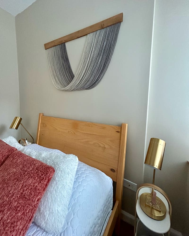 Textile art piece hanging above bed of studio apartment.