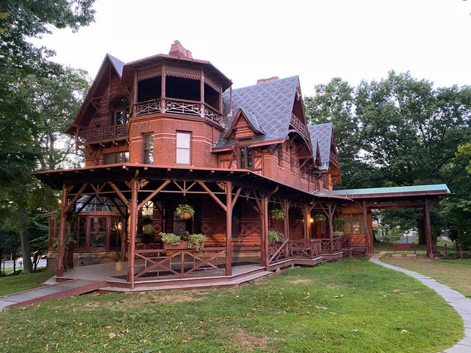 a-brick-red-High-Victorian-Gothic-house-with-a-wrap-around-porch-and-surrounded-by-trees