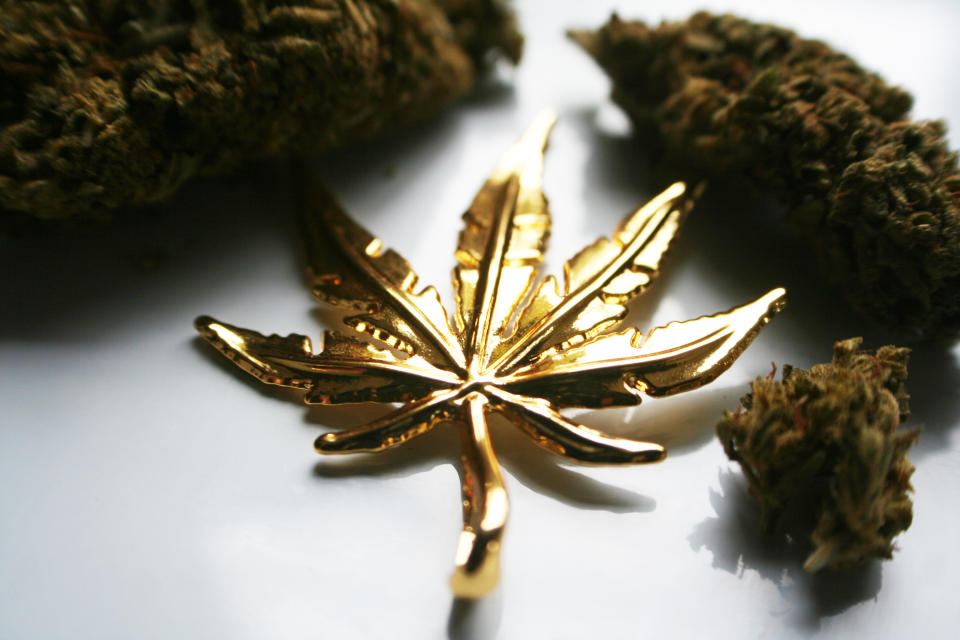 A gold marijuana leaf on a table beside marijuana buds.