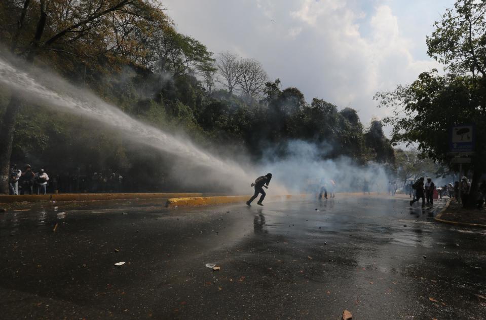 Demonstrators take cover from the water cannon during clashes at a anti-government protest in Caracas, Venezuela, Wednesday, March 12, 2014. According to local authorities, several deaths have been reported and a number of others, including National Guardsmen, have been wounded after being shot by unknown assailants in separate incidents in the central Venezuelan city of Valencia. (AP Photo/Fernando Llano)