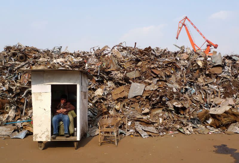 FILE PHOTO: A worker naps in front of scrap metal dump site at a import dock in Taizhou