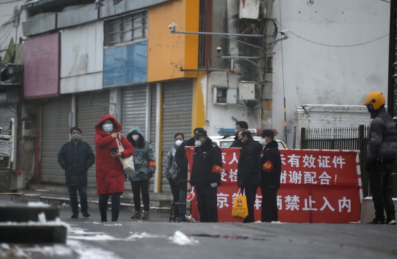 Security personnel and local officials stand guard at an entrance of a residential area for migrant workers in a village on the outskirts of Beijing