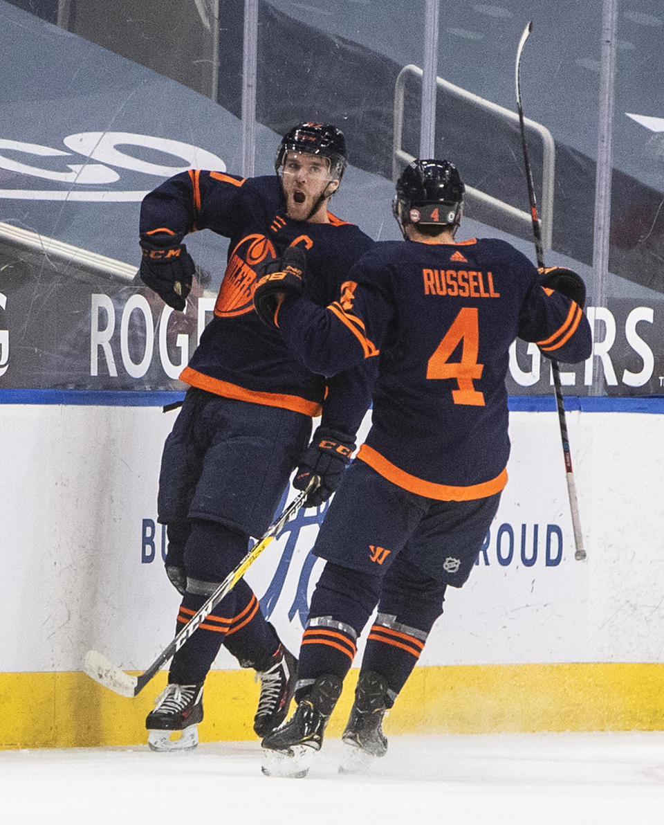 Edmonton Oilers' Connor McDavid (97) and Kris Russell (4) celebrate a goal against the Calgary Flames during the third period of an NHL hockey game Saturday, March 6, 2021, in Edmonton, Alberta. (Jason Franson/The Canadian Press via AP)