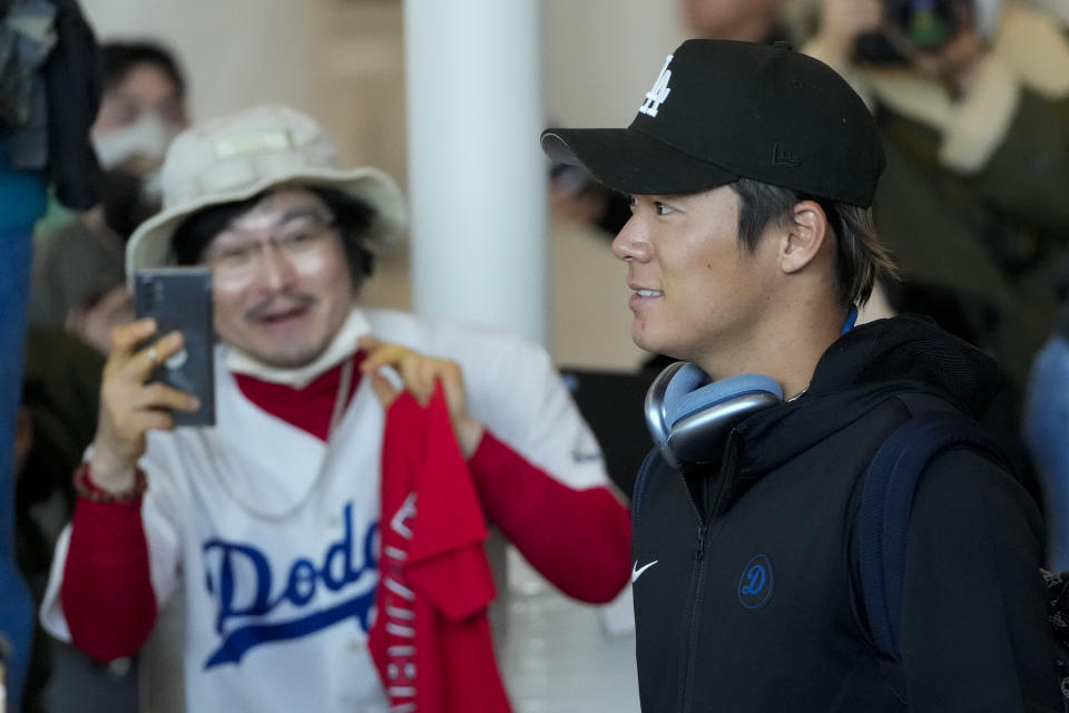 CORRECTS DATE - A supporter, left, wears a Los Angeles Dodgers jersey as pitcher Yoshinobu Yamamoto walks by during the baseball team's arrival at Incheon International Airport, Friday, March 15, 2024, in Incheon, South Korea, ahead of the team's baseball series against the San Diego Padres. (AP Photo/Lee Jin-man)