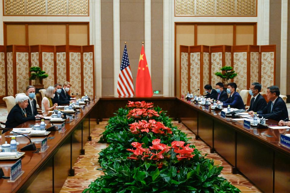 US and Chinese officials stare at each other across a boardroom table with their respective flags in the background.