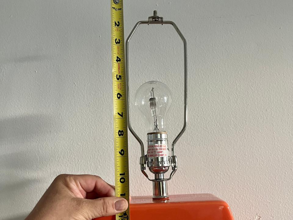 A hand holds a measuring tape up to an orange lamp