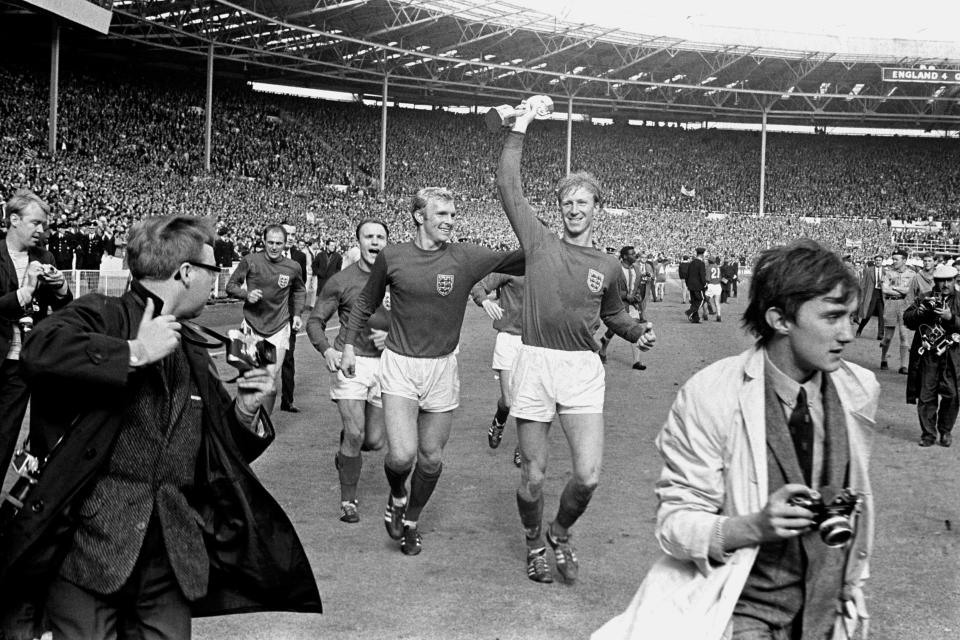 En esta imagen del 30 de julio de 1966, el inglés Jack Charlton sostiene la copa Jules Rimet mientras saluda al público en Wembley acompañado de su compañero Bobby Moore luego de derrotar 4-2 a Alemania Occidental. (PA via AP)