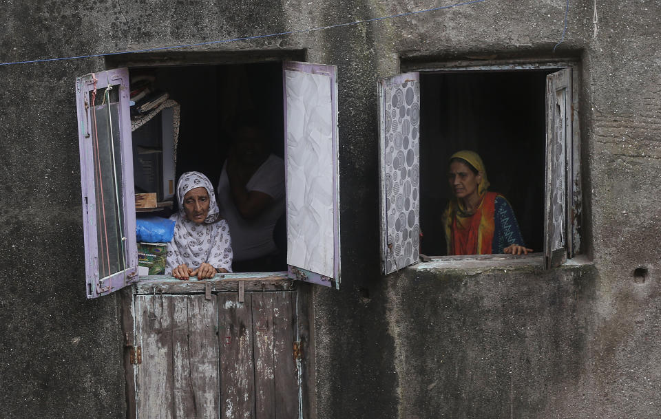 Women look from the windows as rescuers work at the site of a building that collapsed in Mumbai, India, Tuesday, July 16, 2019. A four-story residential building collapsed Tuesday in a crowded neighborhood in Mumbai, India's financial and entertainment capital, and several people were feared trapped in the rubble, an official said. (AP Photo/Rafiq Maqbool)