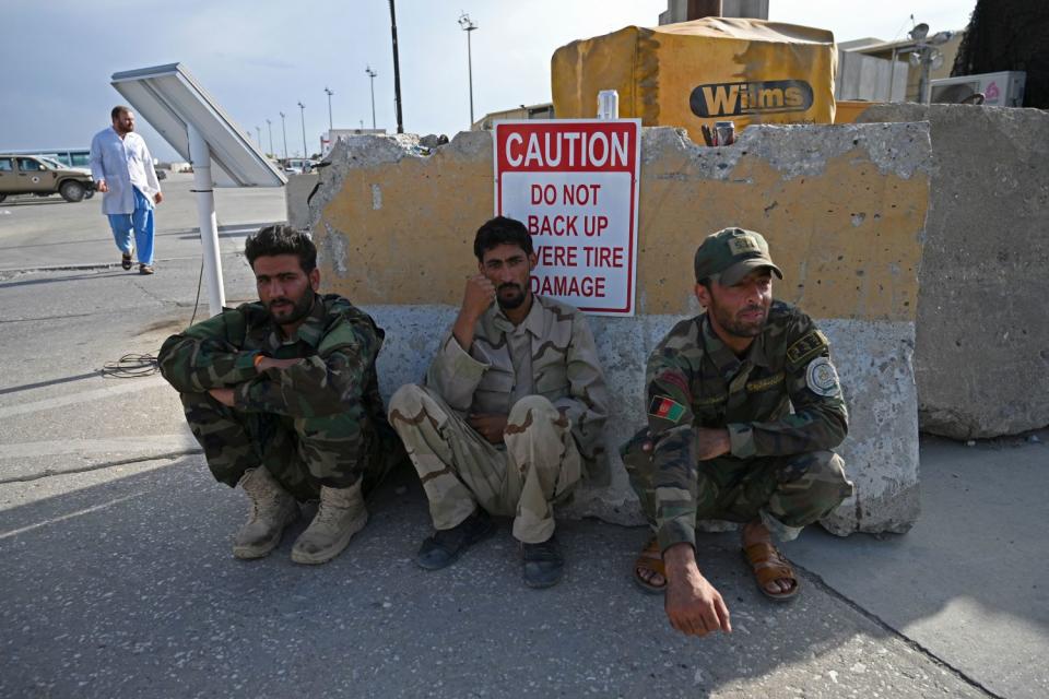 Three Afghan soldiers sit against a battered piece of concrete.