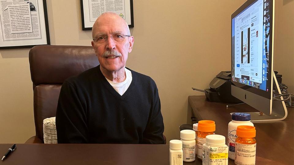 PHOTO: David Mitchell, founder of Patients for Affordable Drugs, sits in his home office. Beside him are some of the many drugs he takes to treat multiple myeloma and other conditions.  (Arthur Allen/KFF Health News)