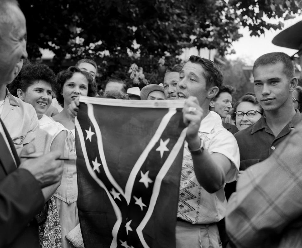 FILE - In this Sept. 3, 1957 file photo, Paul Davis Taylor displays a Confederate flag in front of Little Rock Central High School in Little Rock, Ark. Taylor was among some 500 people who gathered across the street from the school, which had been scheduled to integrate. Five decades and $1 billion after an infamous racial episode made Little Rock a symbol of school segregation, the legal fight to ensure all of its children receive equal access to education has ended. (AP Photo/File)