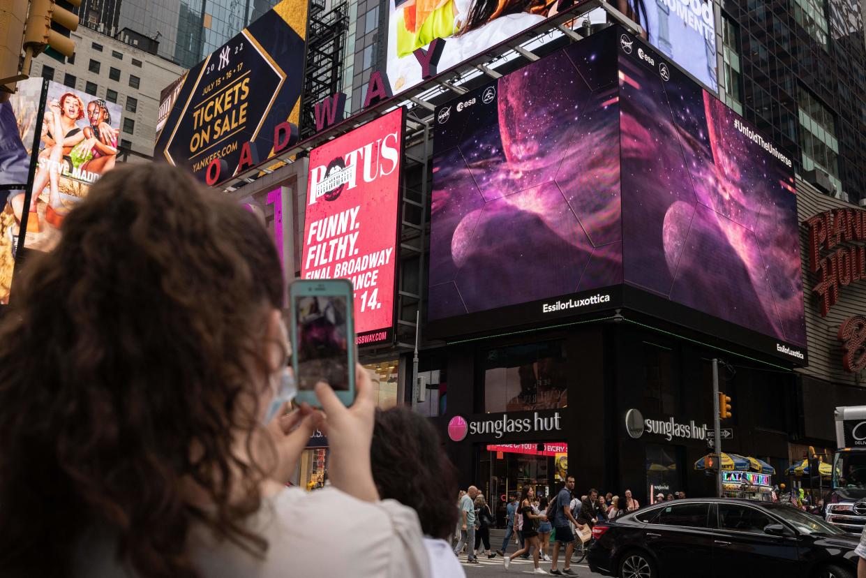 A woman takes a video of the giant screens displaying images captured by the James Webb Space Telescope in Times Square on July 12, 2022 in New York. The state-of-the-art telescope provided researchers with the opportunity to study and unravel the complex chemical composition of a giant gas planet named WASP-107b.