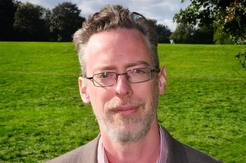 Man in suit jacket in field wearing red rosette