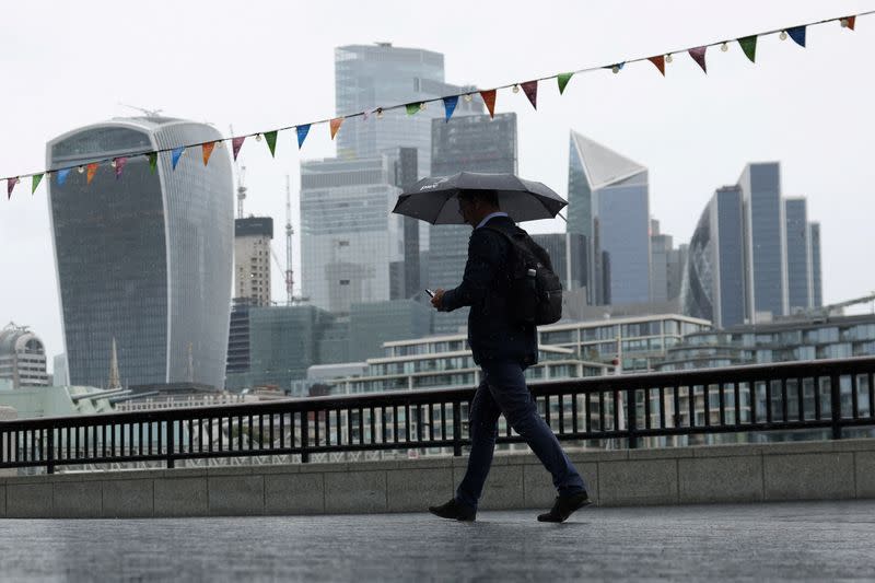 FILE PHOTO: A pedestrian carrying an umbrella walks along the River Thames in view of City of London skyline in London
