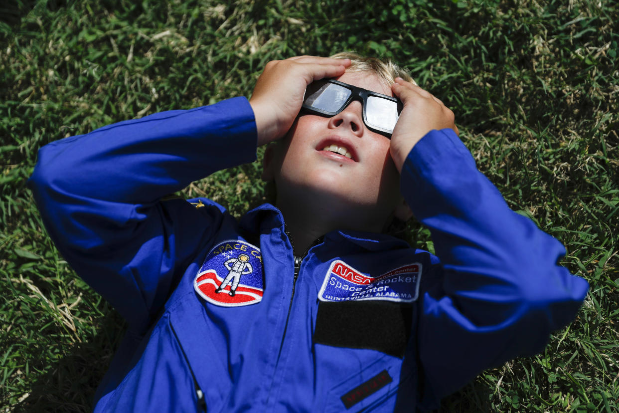 A boy wearing special glasses lies on the grass and looks up to the sky.