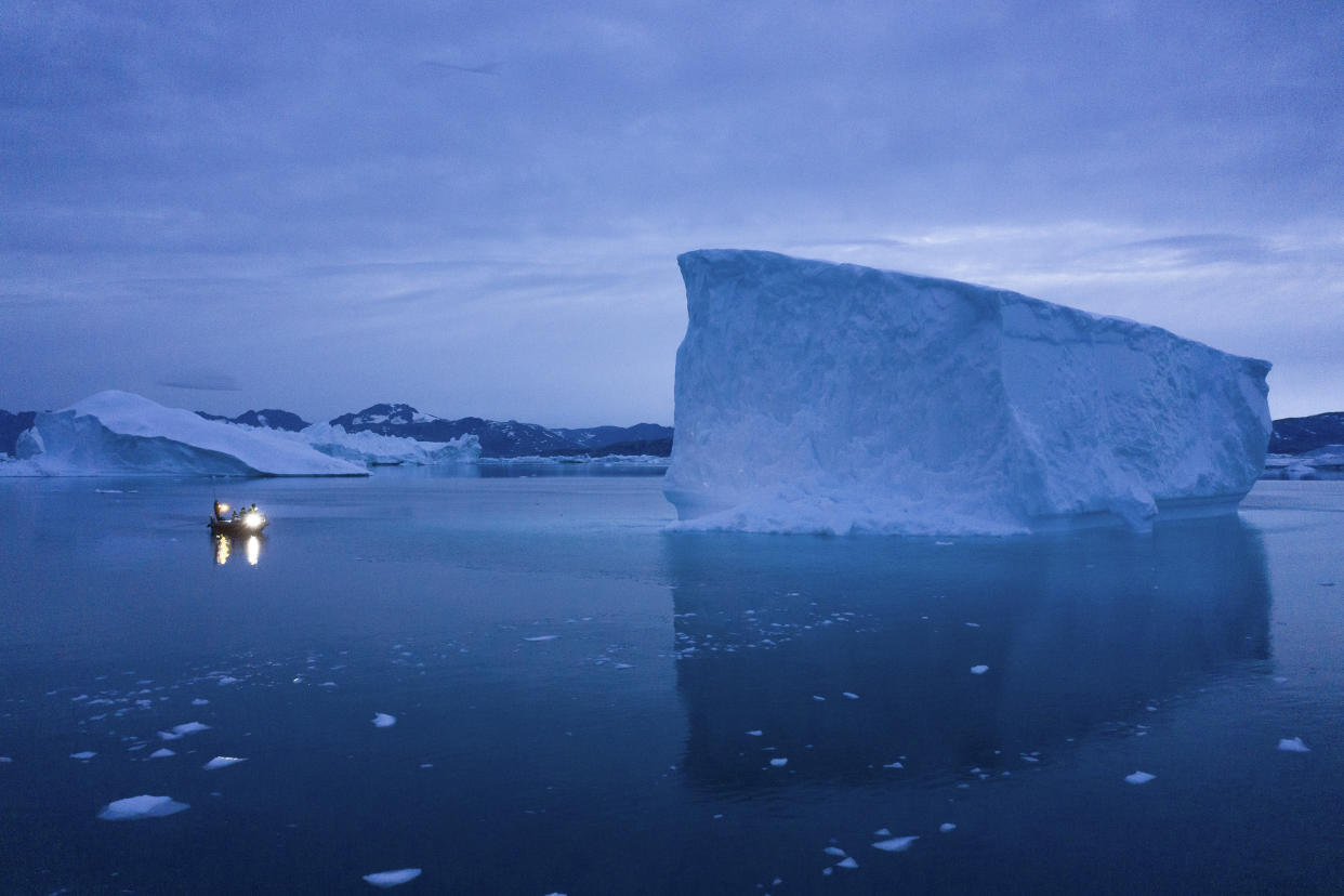 A boat navigates at night near several large icebergs.