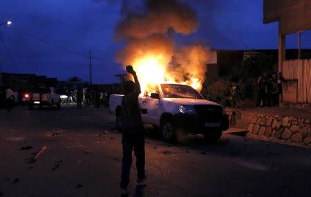 A protester throws stones at a burning car belonging to members of Burundi's police force who were detained by paramilitary officers, accused by civilians for shooting and killing a national military officer, during clashes between protesters and riot police in Burundi's capital Bujumbura April 30, 2015. REUTERS/Thomas Mukoya