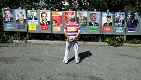 A man looks at campaign posters of the 11th candidates who run in the 2017 French presidential election in Saint Andre de La Roche, near Nice, France, April 10, 2017. L-R : Nicolas Dupont-Aignan, Debout La France group candidate, Marine Le Pen, French National Front (FN) political party leader, Emmanuel Macron, head of the political movement En Marche ! (Onwards !), French Socialist party candidate Benoit Hamon, Nathalie Arthaud, France's extreme-left Lutte Ouvriere political party (LO) leader, Philippe Poutou, Anti-Capitalist Party (NPA) presidential candidate, Jacques Cheminade, "Solidarite et Progres" (Solidarity and Progress) party candidate, lawmaker and independent candidate Jean Lassalle, Jean-Luc Melenchon, candidate of the French far-left Parti de Gauche, Francois Asselineau, UPR candidate, and Francois Fillon, the Republicans political party candidate. REUTERS/Eric Gaillard