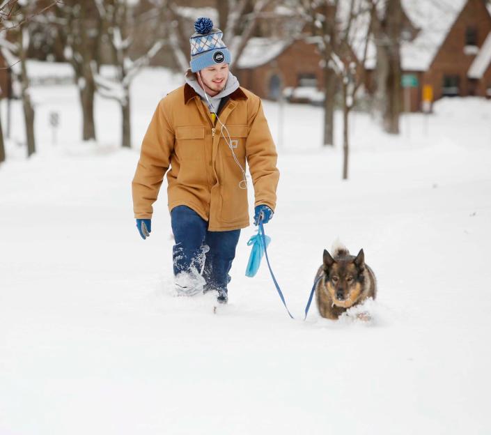 Zach Marzick takes his dog Sage for a walk along a sidewalk covered knee-deep in snow Monday in Akron&#39;s Firestone Park neighborhood.