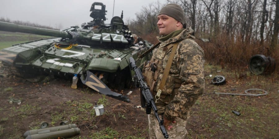 A Ukrainian soldier stands next to a destroyed Russian tank in Donetsk Oblast