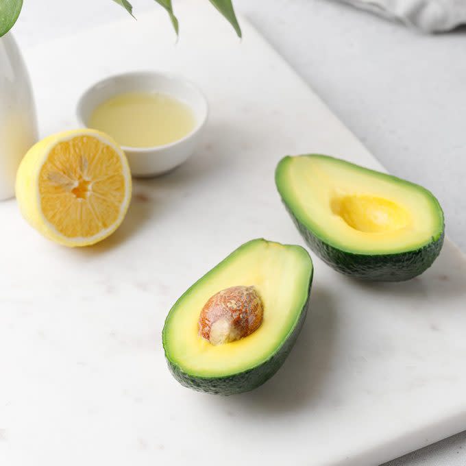 Cut ripe green avocado on a white marble board with vase and lemon juice. Food composition.