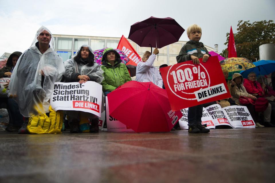 People listen to the top-candidate of the left-wing Die Linke party Gregor Gysi (not pictured) at an election campaign event in Berlin, September 20, 2013. German voters take to the polls in a general election on September 22. The placards read: "Minimum wage instead of Hartz IV", "100% for Peace" and "Sharing is Fun." REUTERS/Thomas Peter (GERMANY - Tags: POLITICS ELECTIONS)