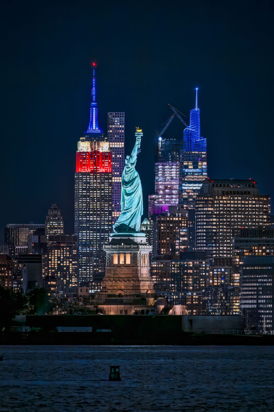 new york city october 16, 2023 view of the statue of liberty in new york harbor with the empire state building lit up in red, white and blue colors the statue is a large neoclassical sculpture on liberty island in new york harbor the copper statue was a gift from the people of france and was designed by french sculptor fredric auguste bartholdi its metal framework was built by gustave eiffel the statue was dedicated on october 28, 1886