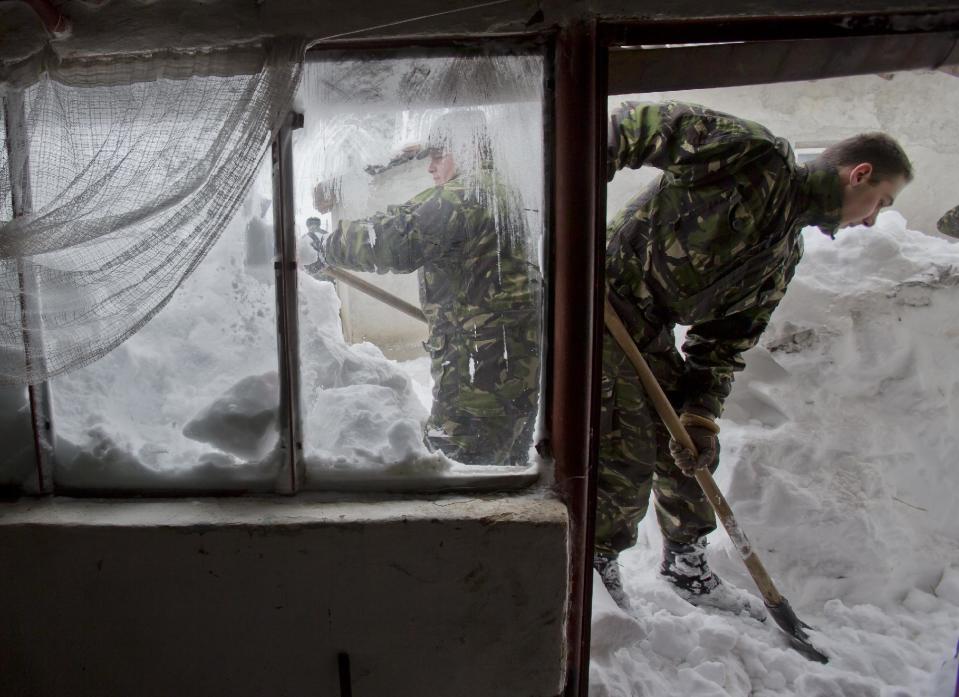 Romanian soldiers clear snow from around an old house in the village of Vadu Pasii, Romania, Tuesday, Jan. 28, 2014. Snow storms are forecast for the coming days in the already affected southeastern regions of Romania in which road and rail traffic were badly disrupted and the army was called in to assist in the worst hit areas. (AP Photo/Vadim Ghirda)