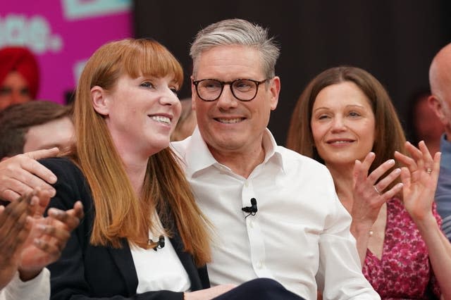 Sir Keir Starmer, seated, with his arm around the shoulder of Labour deputy leader Anglea Rayner, while his wife, Victoria, applauds 