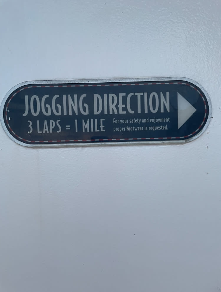 Sign indicating jogging direction with the message: "3 laps = 1 mile. For your safety and enjoyment, proper footwear is requested."