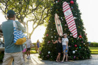 People pose for a photo in front of a Christmas tree at Whalers Village shopping mall on Kaanapali Beach, Wednesday, Dec. 6, 2023, in Lahaina, Hawaii. Residents and survivors still dealing with the aftermath of the August wildfires in Lahaina have mixed feelings as tourists begin to return to the west side of Maui. (AP Photo/Lindsey Wasson)