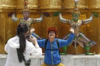A Chinese tourist strikes a similar pose to statues as they visit the Grand Palace in Bangkok March 23, 2015. REUTERS/Chaiwat Subprasom/Files