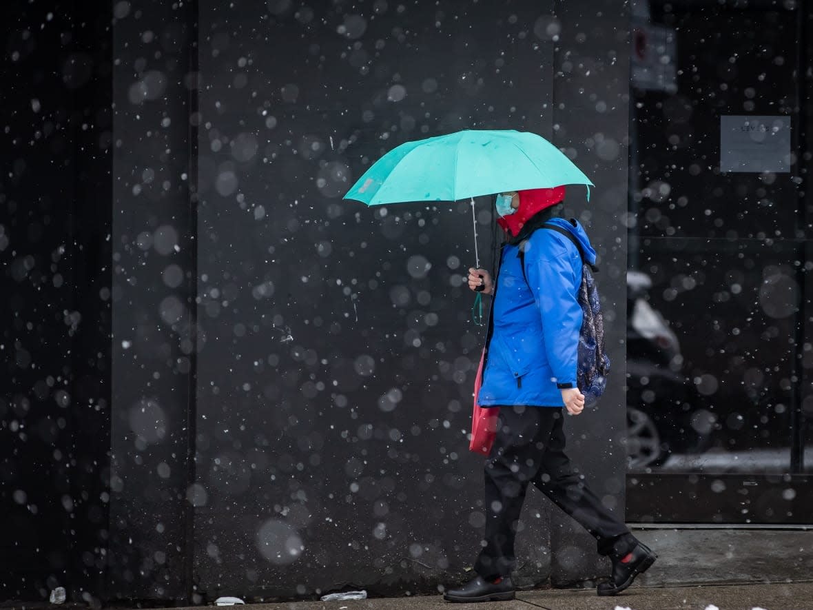 A pedestrian uses an umbrella as snow falls in downtown Vancouver on Saturday, February 13, 2021. The city is currently sitting under a dusting of snow, with the possibility of more to come before nightfall. (Darryl Dyck/The Canadian Press - image credit)