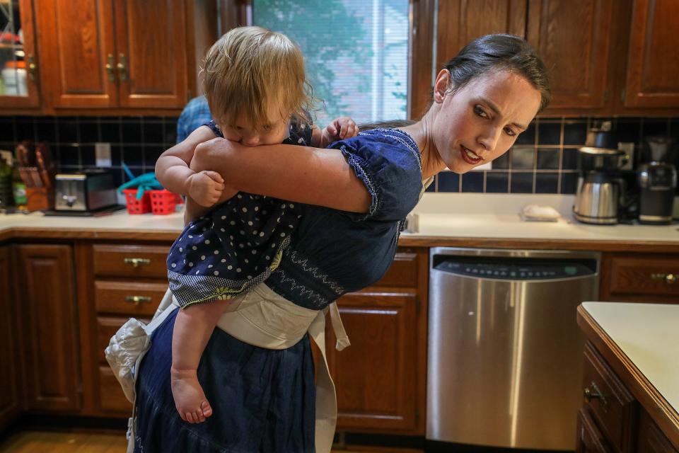Rachael Denhollander straps her daughter, Elora, onto her back so that she can bake a cake with her other children at their former home in Louisville. May 2019