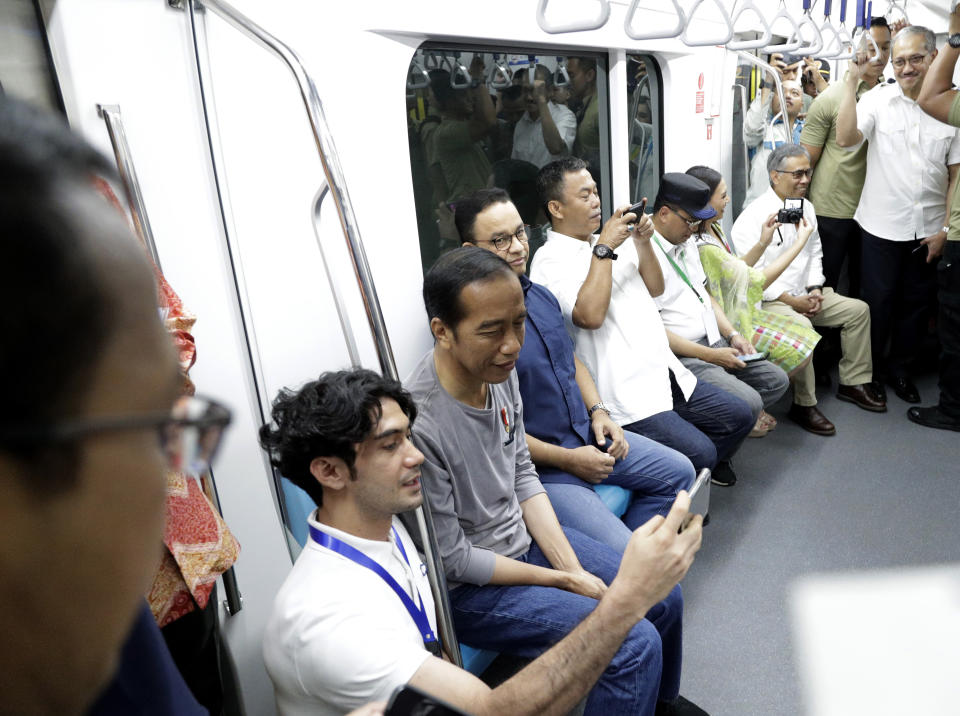 Indonesian President Joko “Jokowi” Widodo, second left, have a selfie taken by Indonesian actor Reza Rahadian, left, as they ride on a Jakarta Mass Rapid Transit train during the inauguration ceremony of the subway line in Jakarta, Indonesia, Sunday, March 24, 2019. The 16-kilometer (10-mile) line system running south from Jakarta's downtown is the first phase of a development that if fully realized will plant a cross-shaped network of stations on the teeming city of 30 million people. (AP Photo/Dita Alangkara, Pool)