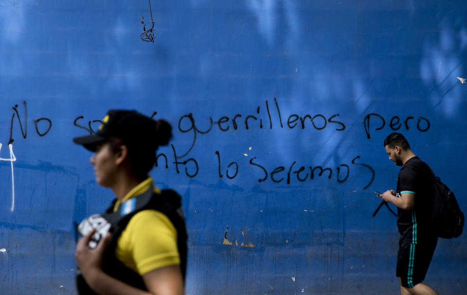 People pass in front of Spanish graffiti: "We are not guerrillas but soon we will be" in downtown Tegucigalpa, Honduras, Saturday, Aug. 24, 2019. U.S. prosecutors say President Juan Orlando Hernández took $1.5 million in drug trafficking proceeds for his campaign to win the presidency in 2013. (AP Photo/Eduardo Verdugo)