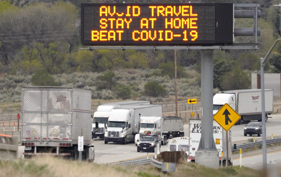 Semi trucks drive by a freeway sign along Interstate 5 that urges people to stay at home due to the COVID-19 outbreak on their way toward Los Angles, Tuesday, March 24, 2020, in Gorman, Calif. (AP Photo/Mark J. Terrill)