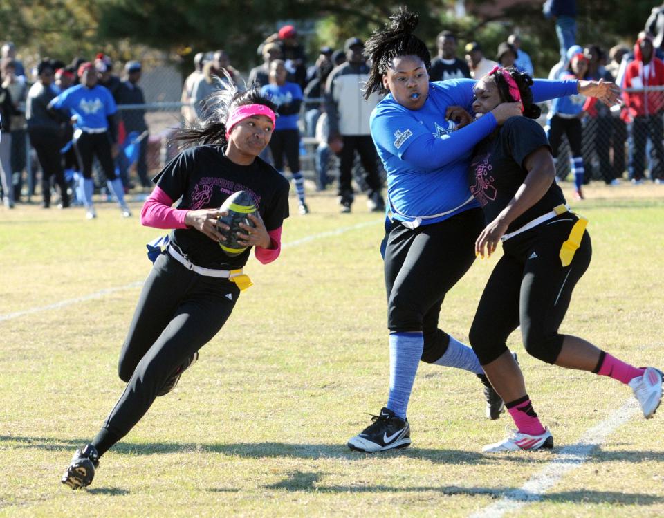 Pink Panthers player Kim Hines runs the ball as the Blue Angels' Uniquah Allen blocks the Pink Panthers' Carla Marshall at the annual Turkey Bowl football game at Williston Field in 2012.