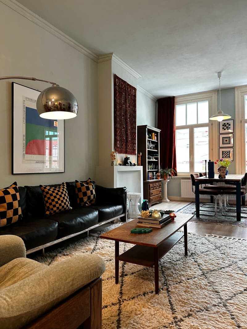 Living room and dining room with black leather vintage sofa, vintage rugs, and vintage art on the walls