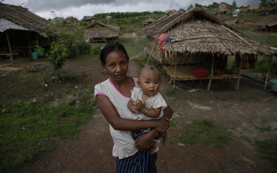 36 year old Mro (a sub-group of Rakhine ethnic people) ethnic woman carrying her 9 months old daughter stands near bamboo-thatch tents - Shutterstock