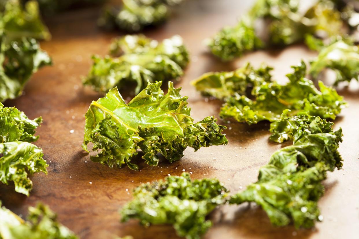 Closeup of several crispy kale "Chips" on a wooden cutting board with a blurred background