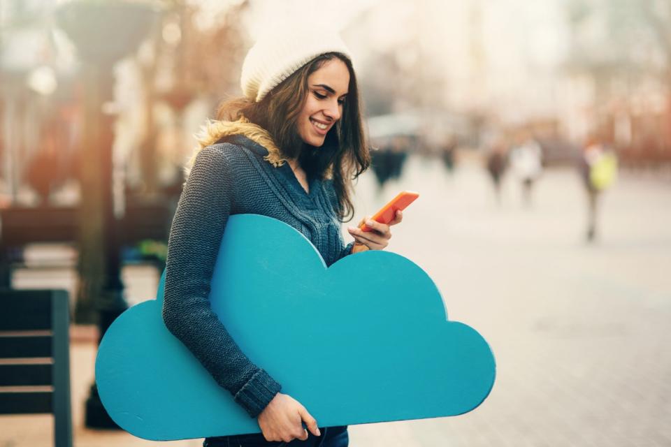 A person checks something on a smartphone while holding a cardboard cutout of a cloud in his hand.