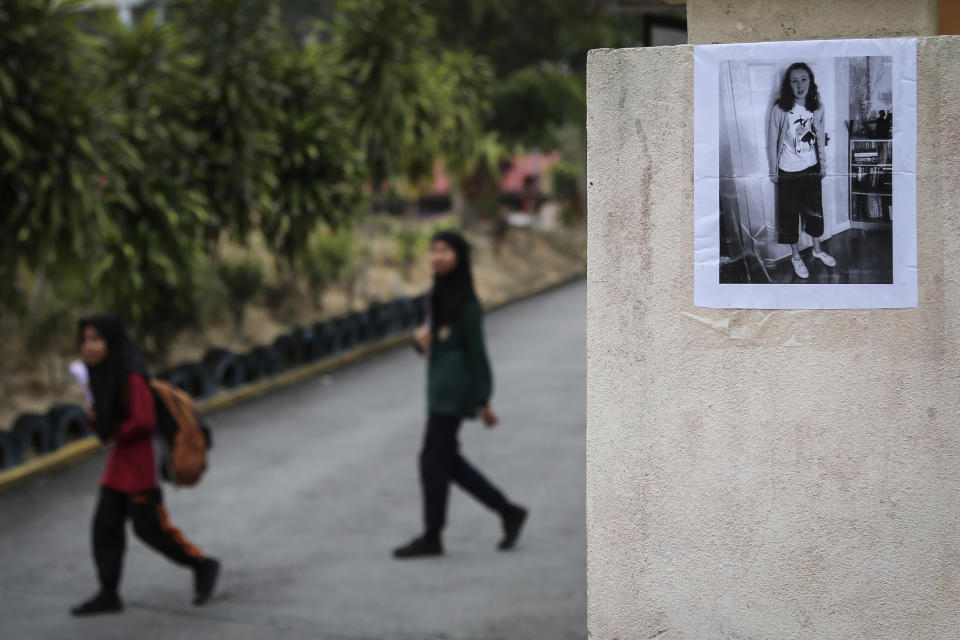 Students walk past a photo of missing British girl Nora Anne Quoirin placed on a pillar outside a school in Seremban, Malaysia, Wednesday, Aug. 7, 2019. Malaysian police said Wednesday that some fingerprints were found in a forest resort chalet where the 15-year-old London girl was reported missing four days ago, and that they do not rule out possible criminal element. (AP Photo/Annice Lyn)