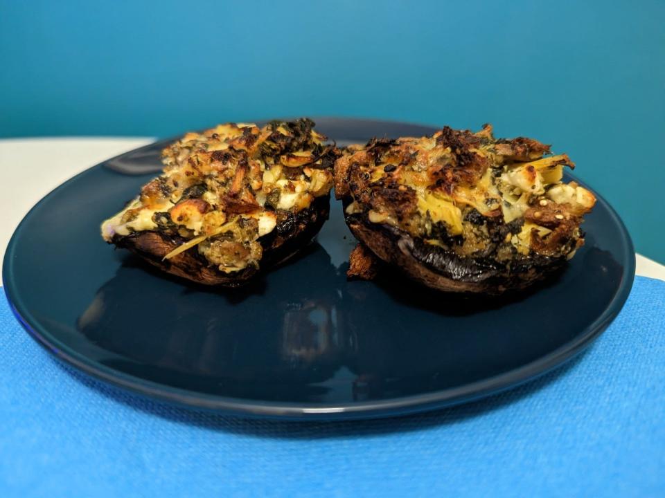 two stuffed portobello mushrooms on a dark plate on a kitchen table